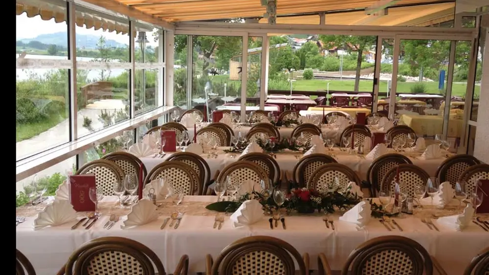 Gedeckte Tafeln vor den Panoramafenstern in der Fischerhütte in Hopfen am See bei Füssen