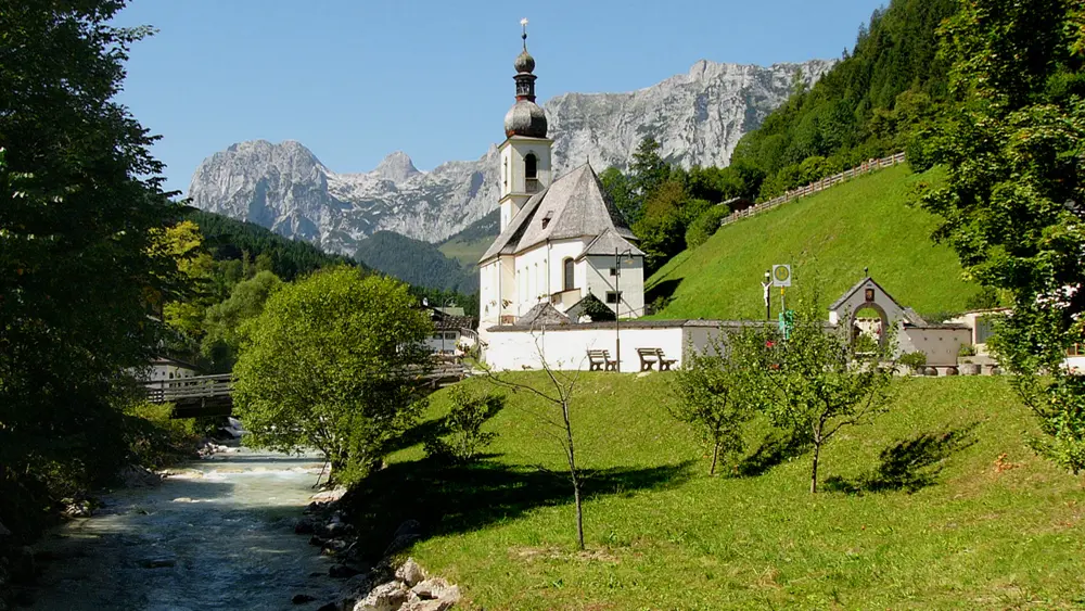 Außenansicht der Pfarrkirche St. Sebastian in Ramsau mit den Bergen im Hintergrund