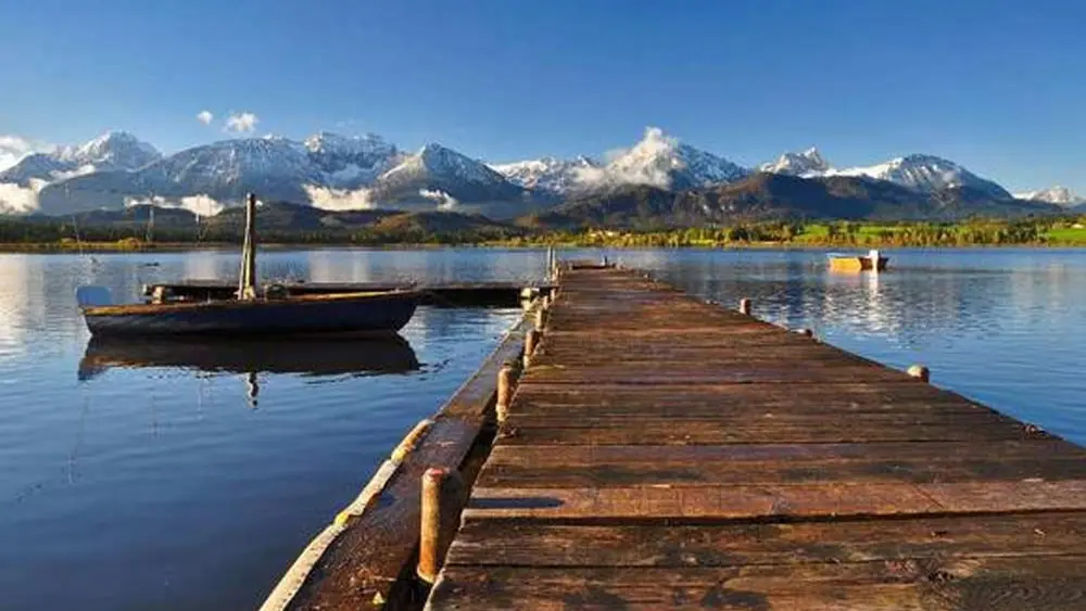 Blick von einem Holzsteg auf den Hopfensee, im Hintergrund die Allgäuer Alpen