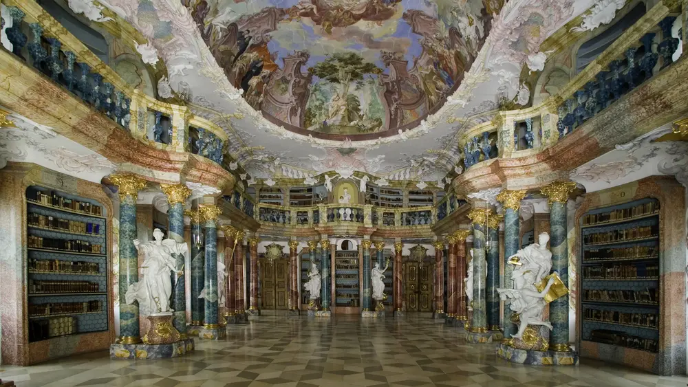 Der Bibliothekssaal ist ein Meisterwerk des Rokoko und begeistert mit seiner schwingenden Raumform, reichem Figurenschmuck und einem Deckenfresko.