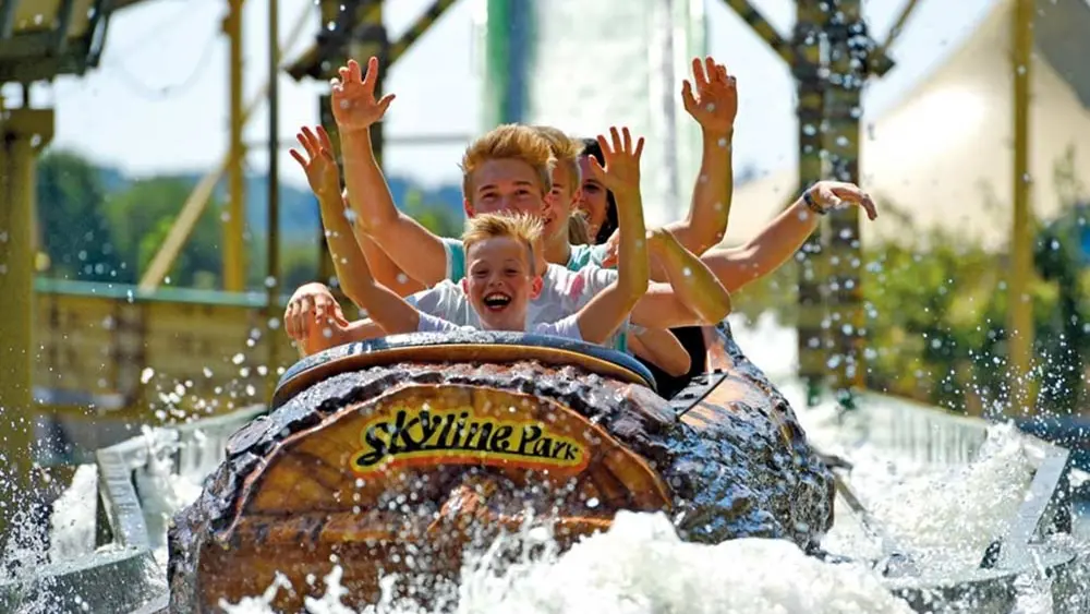 Eine Familie sitzt in einem der Baumstammboote der Wildwasserbahn im Allgäu Skyline Park
