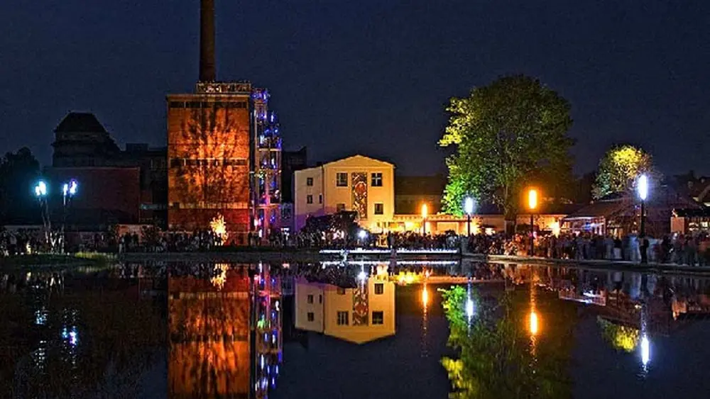 Blick über den See auf die beleuchtete Promenade im Auenpark Martredwitz