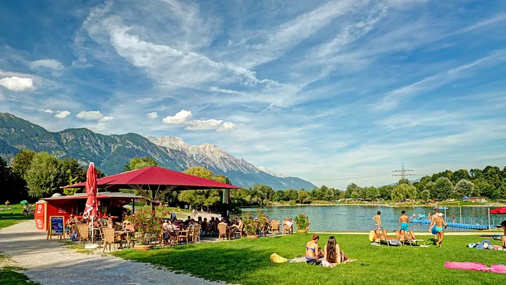 Westufer des Badesees Rossau bei Innsbruck mit Schwimmsteg und Liegewiese