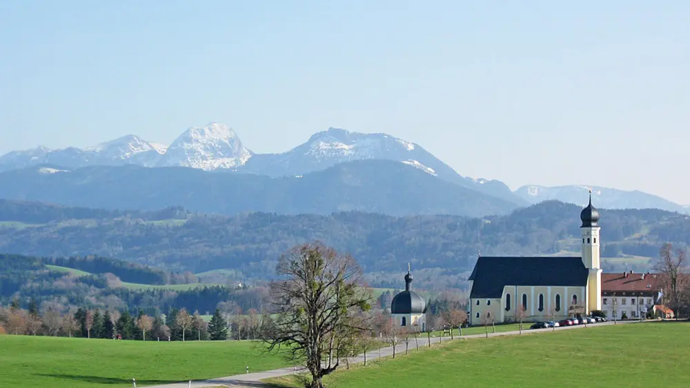 Blick auf die Wallfahrtskirche Wilparting St. Marinus vor dem Mangfallgebirge in Irschenberg