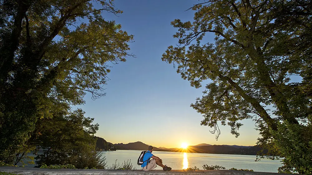 Wanderer sitzt bei Sonnenuntergang am Ufer des Wörthersees