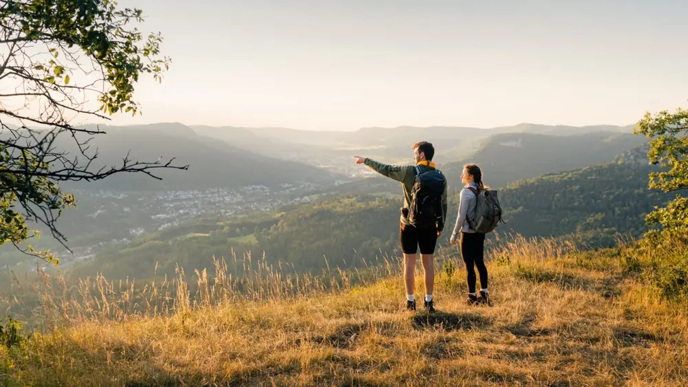 Zwei Wandernde stehen früh morgens an der Albtraufkante und blicken in die Ferne.