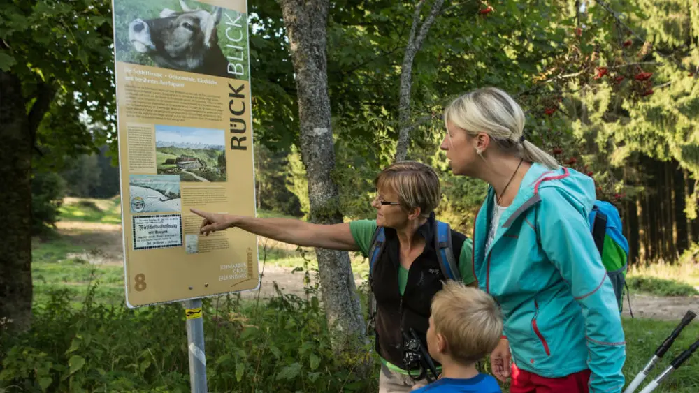 Familie an einem Informationsschild des Schwarzen Grat Erlebniswegs in Isny