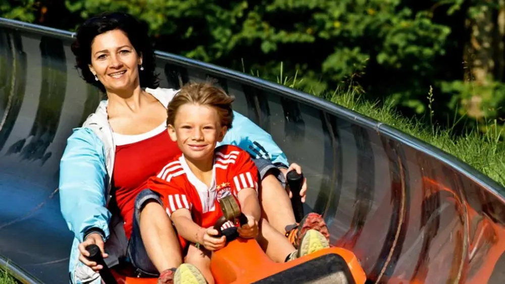 Eine Frau und ein Kind fahren in einem Bob die Sommerrodelbahn am Hündle hinab