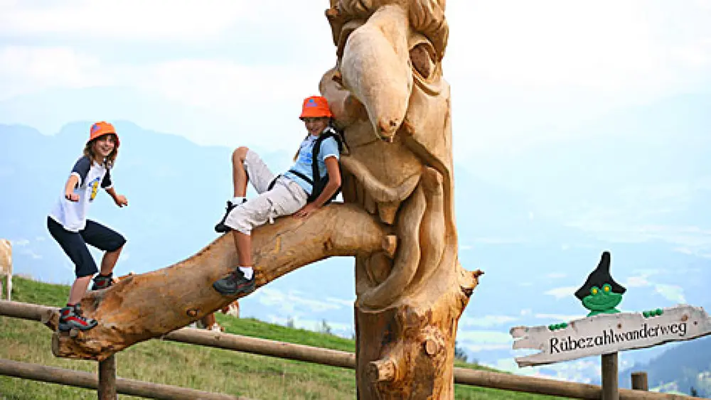 Kinder auf einer Schnitzfigur am Rübezahl-Wanderweg bei Ellmau