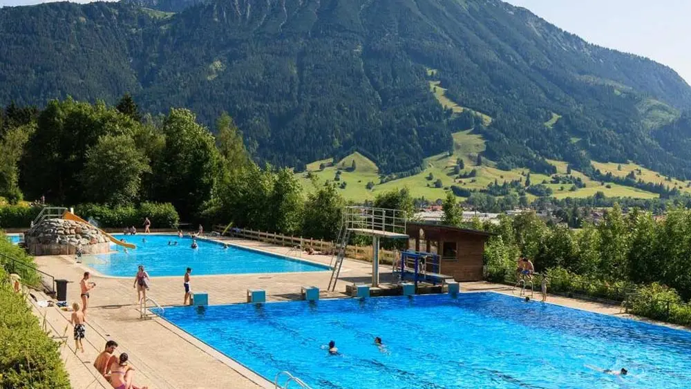 Badegäste im Außenbecken des Alpenbads Pfronten, im Hintergrund das Tal und die Berge