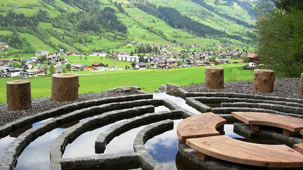 Blick auf das Wasserlabyrinth am Wohlfühlweg Westendorf, im Hintergrund Westendorf und Berge