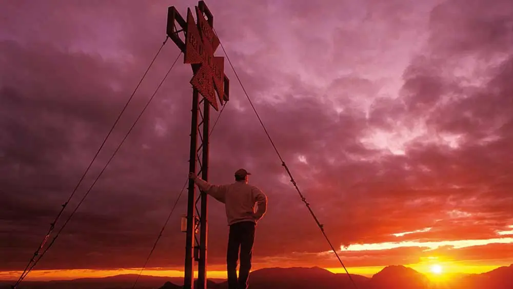 Wanderer bei Sonnenuntergang an einem Gipfelkreuz im Geopark Karawanken