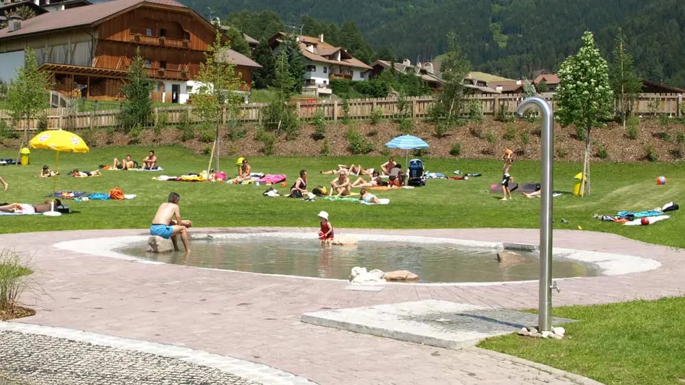 Blick auf das Kleinkinderbecken, die Liegewiese und die Dusche am Toblacher Naturbadesee
