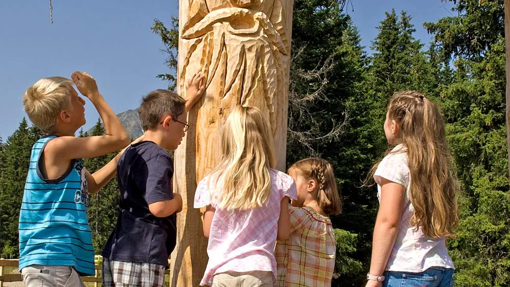 Kinder vor einem geschnitzten Baumbart auf dem Oberperfer Geisterwanderweg in Oberperfuss