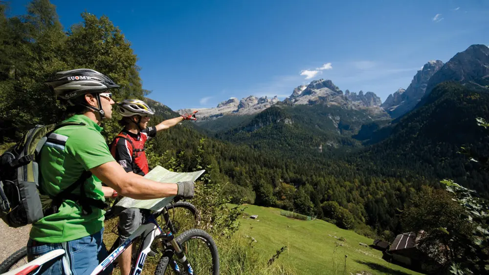 Zwei Mountainbiker mit Karte und Blick auf die Berge im Naturpark Adamello-Brenta
