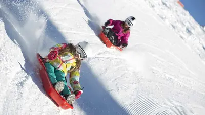 Kinder beim Rodeln mit Rutschwannen in Alpe d'Huez