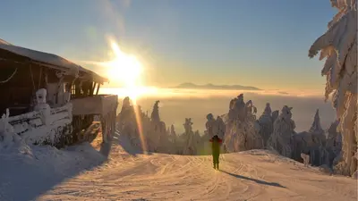 Piste mit Hütte und Skifahrer im Sonnenaufgang