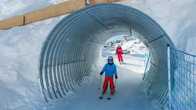 Ein Kind fährt durch einen Tunnel auf der Family Funslope auf der Fischeralp