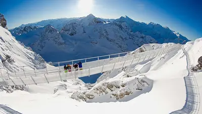 Vier Wintersportler genießen die Aussicht auf der Hängebrücke Cliffwalk in Titlis