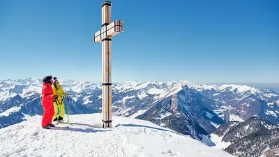 Skifahrer an einem Gipfelkreuz im Skigebiet Diedamskopf