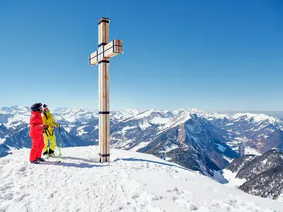 Skifahrer an einem Gipfelkreuz im Skigebiet Diedamskopf © Diedamskopf Alpin Tourismus GmbH & Co KG, Foto: Alex Kaiser