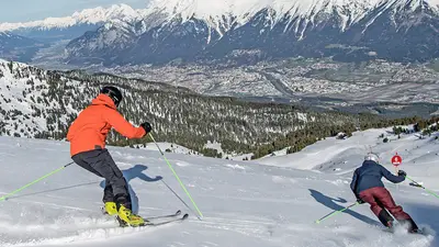 Zwei Skifahrer bei der Abfahrt mit Blick auf den Ort
