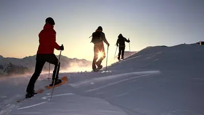 Drei Schneeschuhwanderer bei Sonnenuntergang