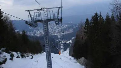 Sessellift zwischen Tannen mit der schweren Piste darunter