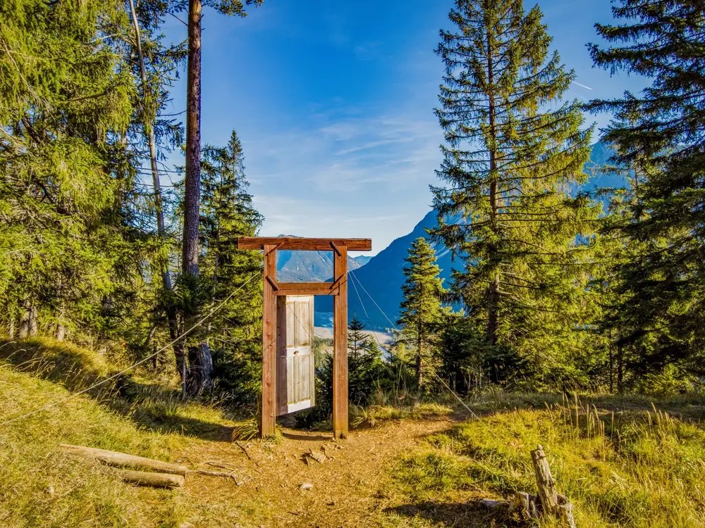 Sonniger Blick mit blauem Himmer auf den Baichlstein durch eine am Wegrand stehende Holztür Porta Alpina