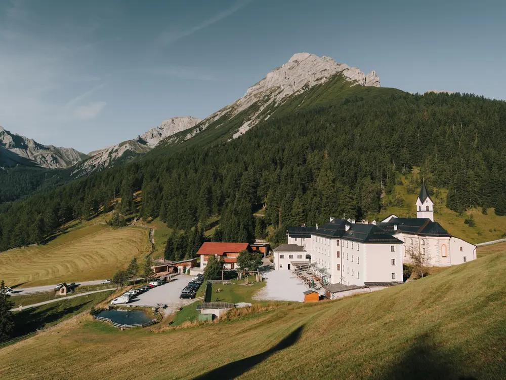 Berge, Wald, Bäume, Wiese, Wahlfahrtskloster, Autos stehen am Parkplatz, Straße, Kloster & Natur Resort Maria Waldrast am Fuß der Serles im Sommer