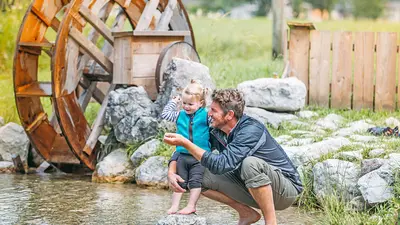 Vater mit Tochter vor einem Wasserrad am Moosbach im Salzburger Saalachtal