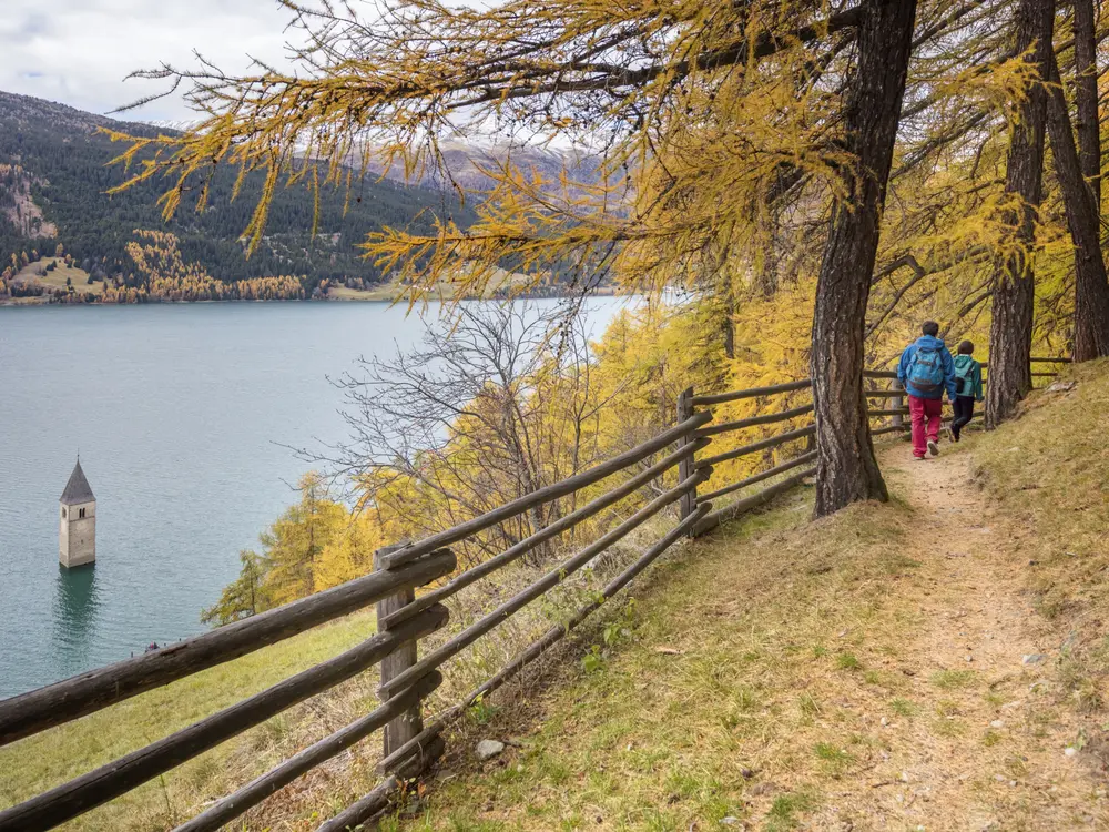 Wandern auf dem Vinschger Hoehenweg mit Blick auf den Kirchturm im See von Alt-Graun