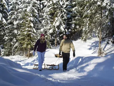 Paar mit Rodel spaziert durch den Schnee in Reutte © Naturparkregion Reutte/Robert Eder