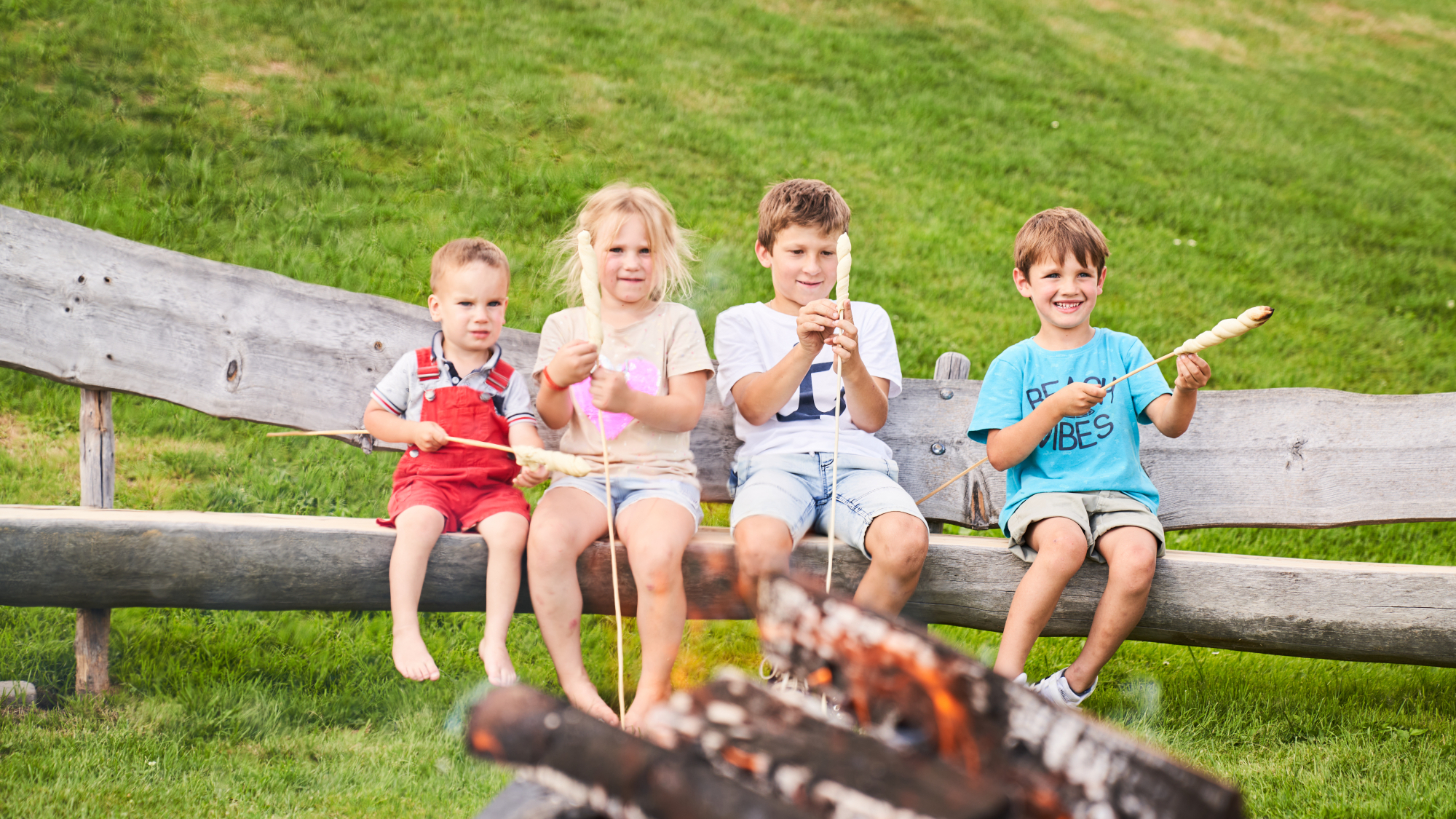 Kinder sitzen am Lagerfeuer mit Steckerlbrot