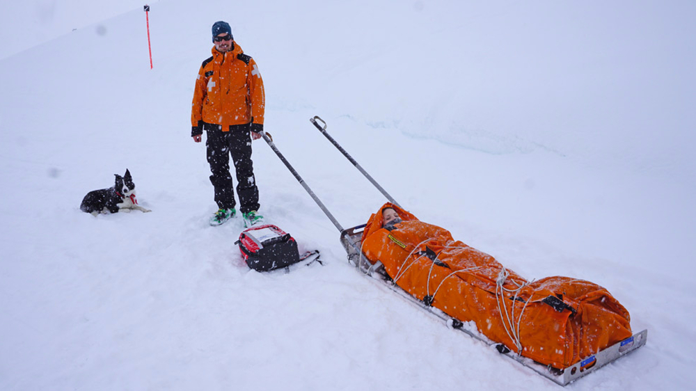 Verschnürter Patient auf dem Rettungsschlitten mit Pistenretter Nico und Chico