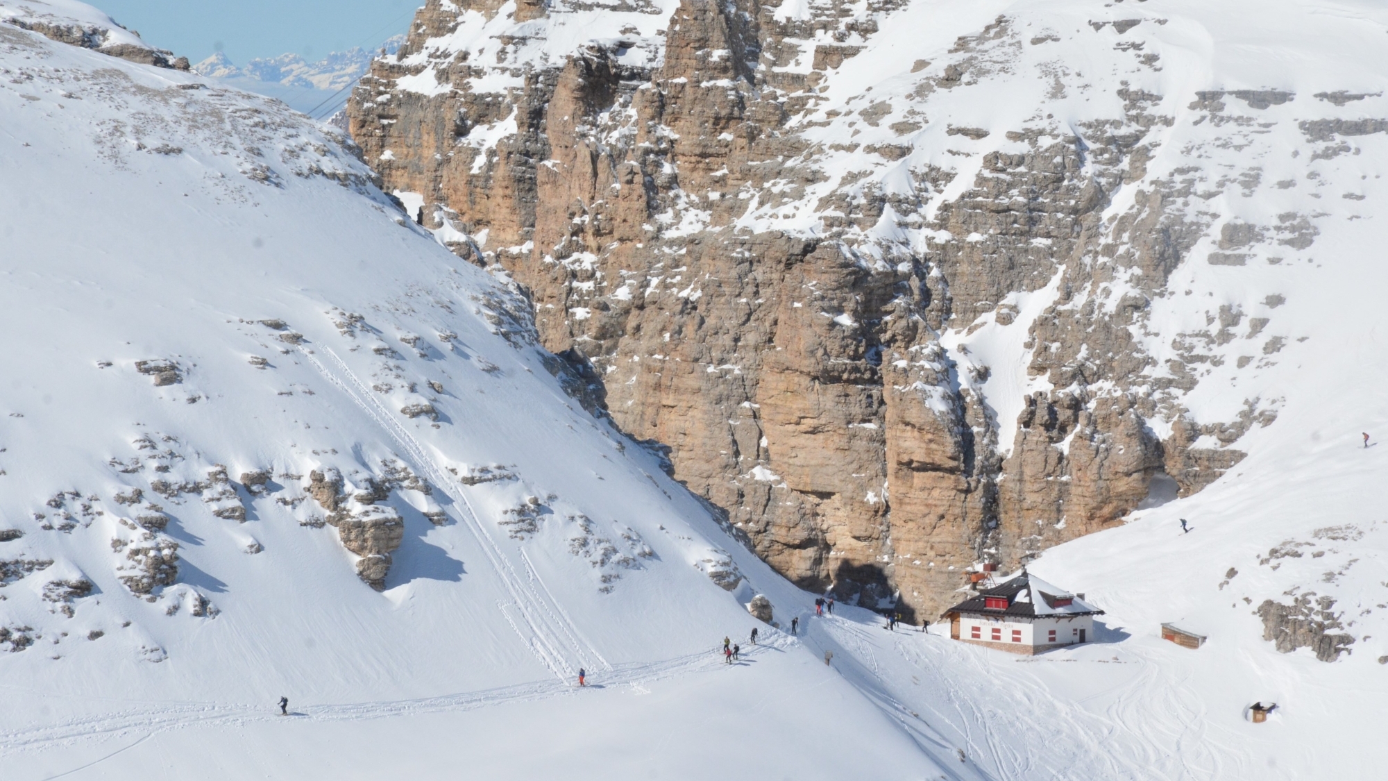 Die Pordoihütte in der Pordoischarte (2848 m). Links davon beginnt die Abfahrt durch die Pordoischarte zum Pordoijoch, rechts davon die Abfahrt durch das Val Lasties zur Dolomitenstraße beim Hotel Lupo Bianco (4 km von Canazei entfernt); die Personen im Bild bewegen sich in Richtung Mittagstal (Val di Mesdi).