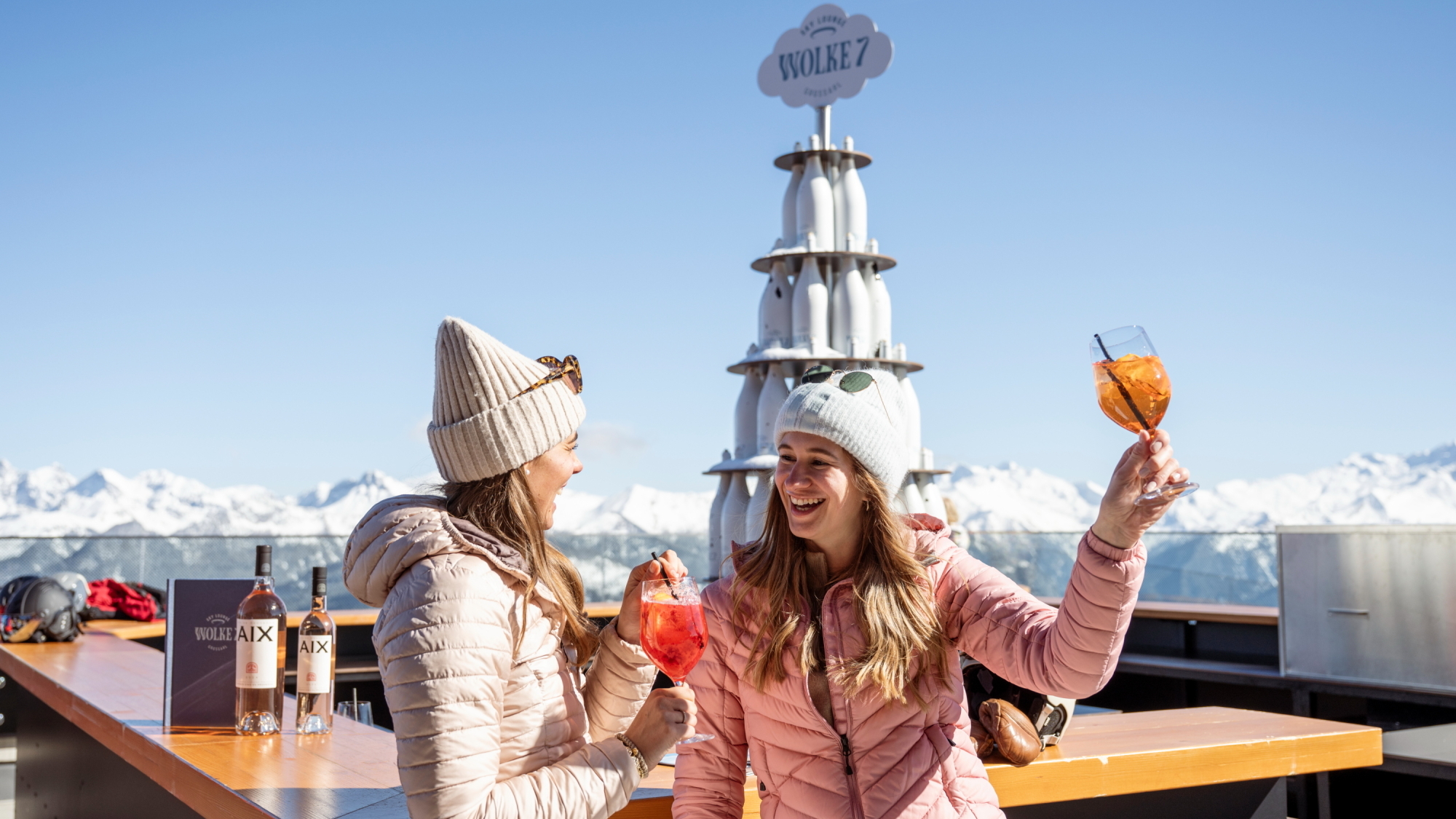 Zwei Damen feiern mit einem Glas Aperol in der Hand vor herrlicher Bergkulisse.