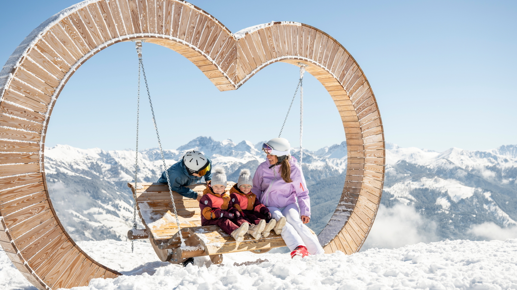 Familienrast beim Skifahren auf einer herzförmigen Schaukel am Berg.