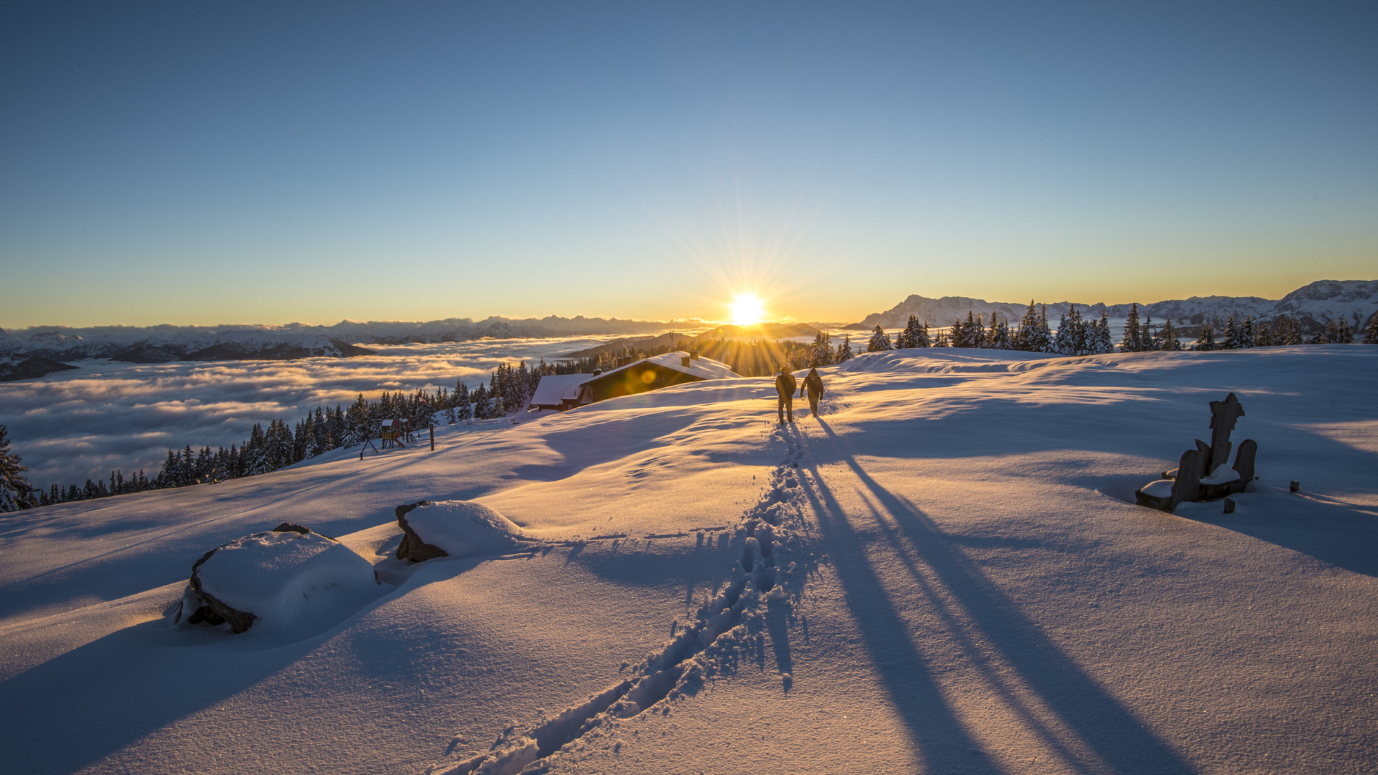 Zwei Wanderer im Schnee bei Sonnenuntergang in den Bergen.