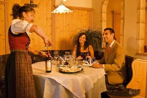 Eine Servicekraft öffnet einem Pärchen am Tisch eine Flasche Wein im Restaurant vom  Hotel Tonnerhof