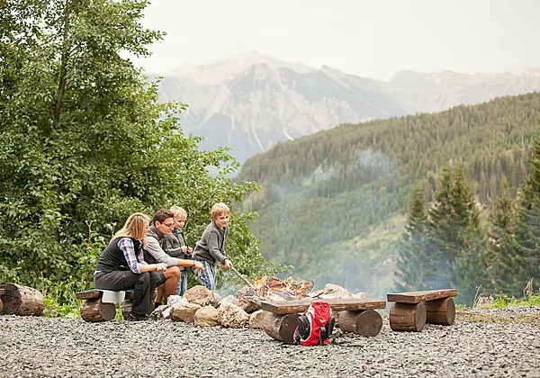 Eine Familie mit Kind am Lagerfeuer vor traumhafter Bergkulisse